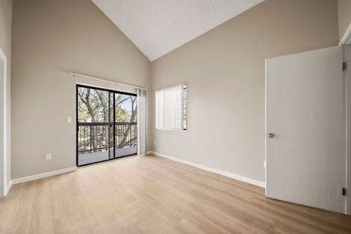 A room with a slanted ceiling, a door, and a window with a view of a tree.