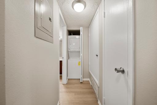 A white hallway with a refrigerator and a door on the right.
