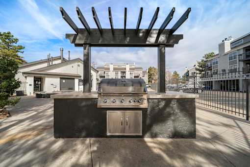 Aurora, CO, Apartments with an In-Unit Washer and Dryer - The Juliet at Lowry - Grilling Station with a Built-In Stainless Steel Grill, Countertop, Black Pergola, and Black Metal Fence.
