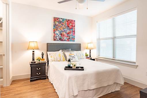 A bedroom with a large bed, a painting above it, and two lamps on either side of the bed.