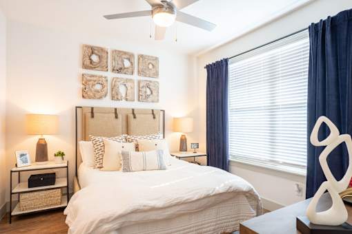 A bedroom with a large bed, a ceiling fan, and a nightstand with a lamp.