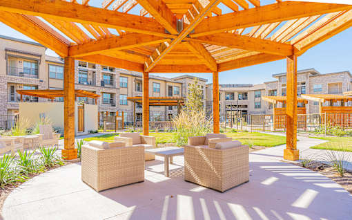 A wooden pergola with wicker chairs underneath it.