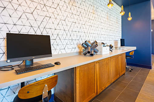 A white desk with a black monitor and keyboard sits against a wall with a geometric pattern.