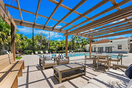 A wooden pergola over a poolside seating area.