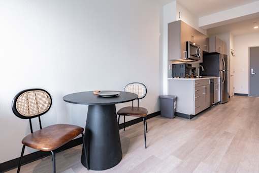 A black table with a plate on it and two chairs with a white wall in the background.