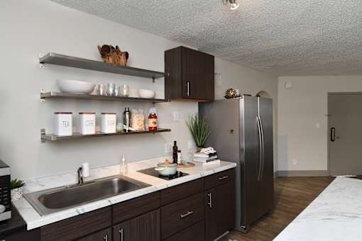 A kitchen with a sink, refrigerator, and shelves with various items.