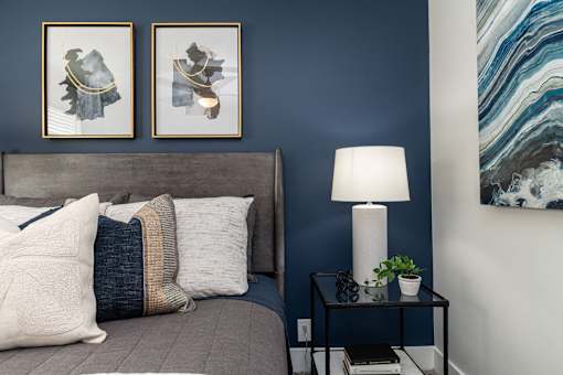 Pet-Friendly Apartments In Hendersonville, TN – Reserve at Drakes Creek-A bed with a grey headboard and a white lamp on a small table.