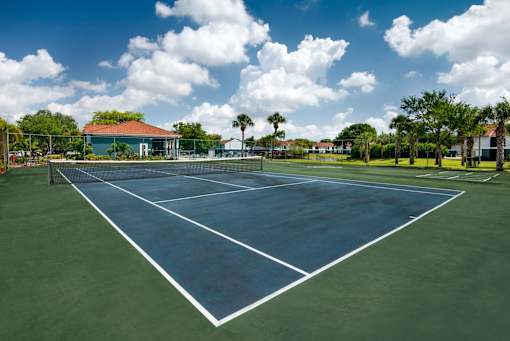 A tennis court with a blue sky and clouds in the background.
