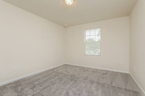A room with a carpeted floor and a window with blinds.