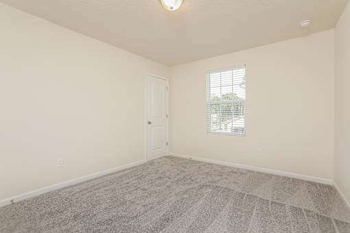 A room with a carpeted floor and a window with blinds.