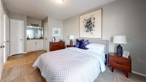 Bedroom at Broad on the Green in Augusta, GA, featuring carpet flooring and a mirror sink with cabinets in a pet-friendly apartment community.