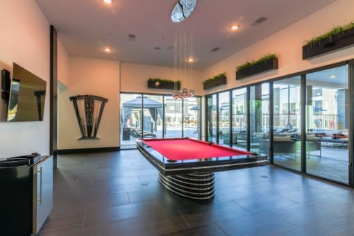 A game room with a red pool table and tv and glass windows and mini fridge