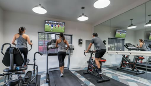 A gym with people exercising and a TV screen showing a soccer game.