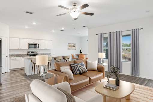 A modern living room with a brown leather couch and a white kitchen in the background.