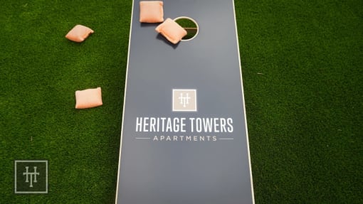 a tennis court with chairs on the grass and the heritage towers apartments logo