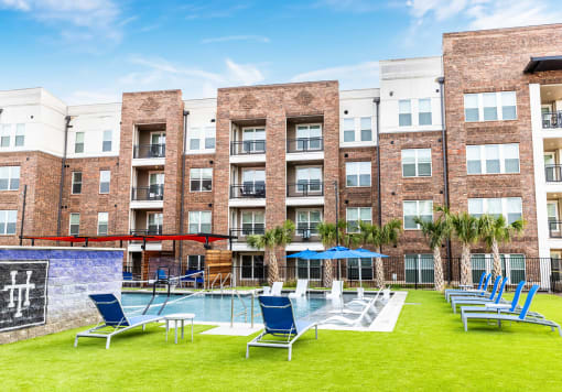 an outdoor pool with lounge chairs and tables in front of an apartment building