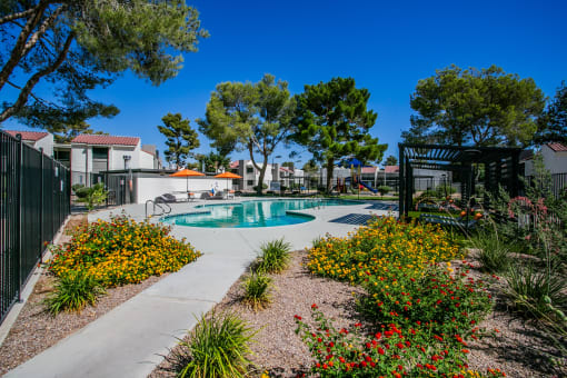 a pool is surrounded by flowers and trees and a fence