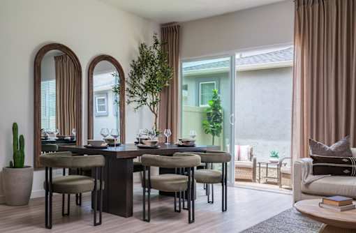 A dining room with a table set for six with a view of a balcony outside.