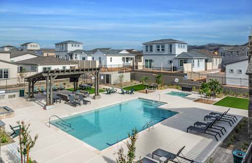 A large swimming pool surrounded by a patio with lounge chairs and a pavilion.