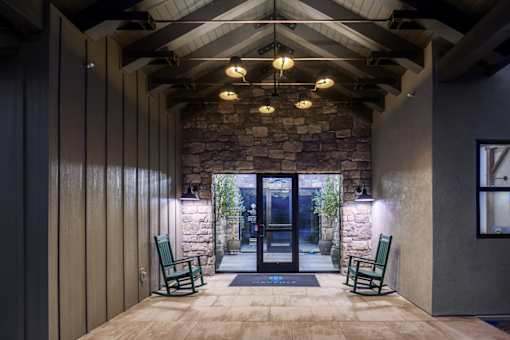 A stone wall with a glass door and two green chairs.