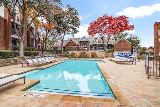 A large outdoor swimming pool surrounded by lounge chairs and trees.