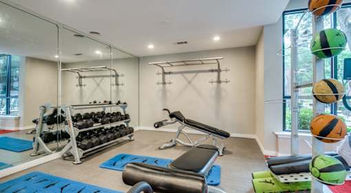 A gym with a variety of equipment including dumbbells, weight plates, and a bench press.