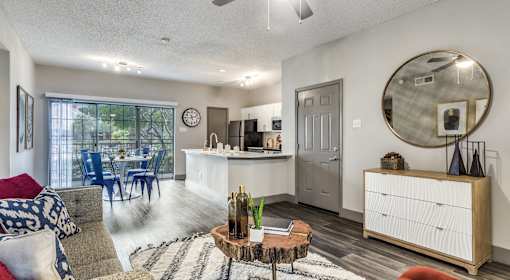A living room with a grey couch, a wooden coffee table, and a round mirror on the wall.