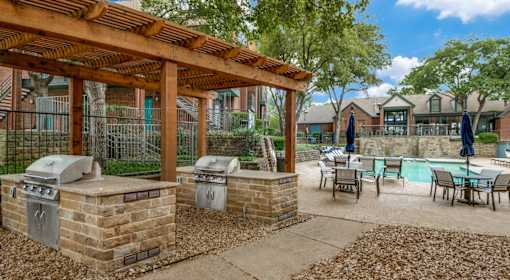 A patio with a grill and a table with chairs.