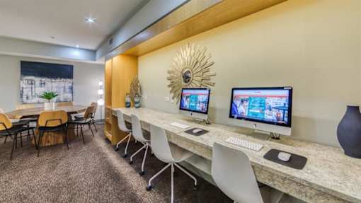A room with a desk, chairs, and computer monitors.