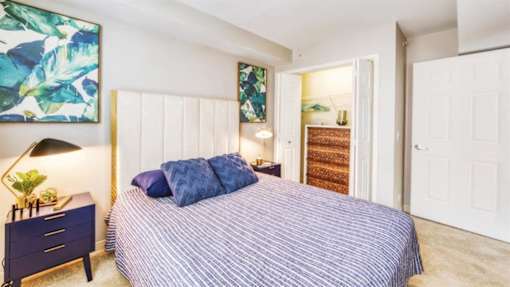 A bedroom with a bed, nightstand, and a painting on the wall.