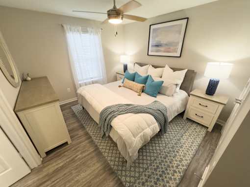 Twin Oaks Apartments in Hattiesburg Mississippi A bedroom with a large bed, a ceiling fan, and a window with white curtains.