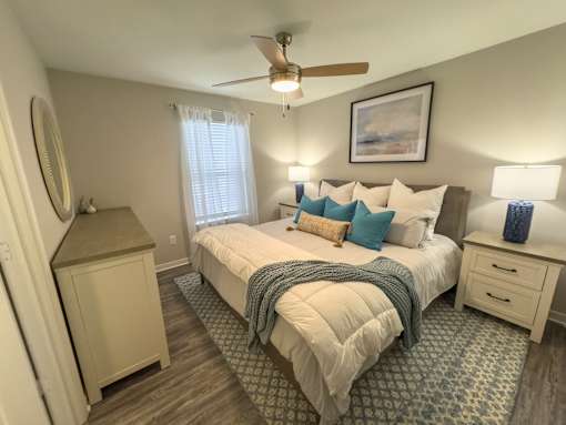 A bedroom with a large bed, a ceiling fan, and a nightstand.