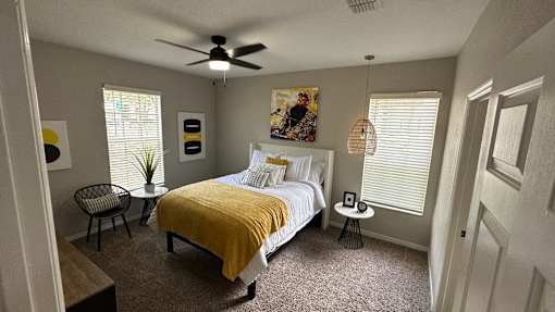 A bedroom with a bed, chair, and a ceiling fan.