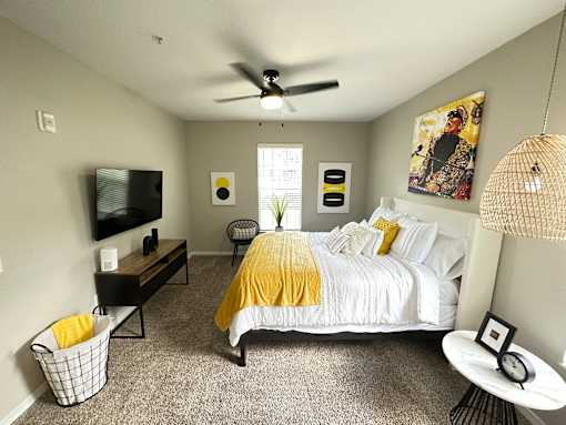 A bedroom with a bed, a TV, a chair, a table, and a ceiling fan.