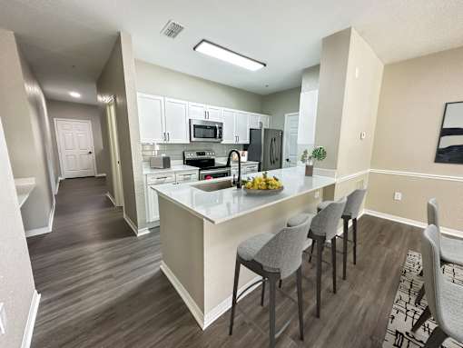 A kitchen with a white island and grey chairs.