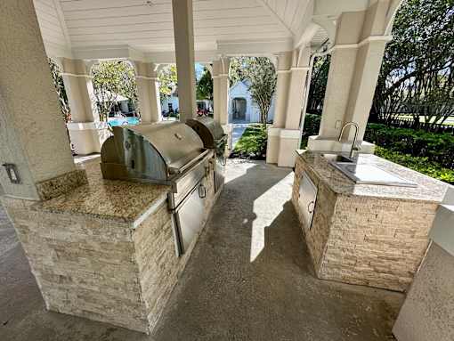 A patio with a grill and sink under a roof.