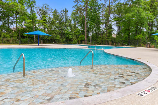 a swimming pool with a fountain in the middle of it and trees in the background