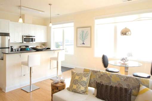 A modern kitchen with a white countertop and a white couch with yellow and brown pillows.