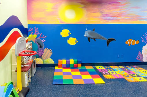 A colorful children's play area with a basketball hoop and a mural of an ocean scene.