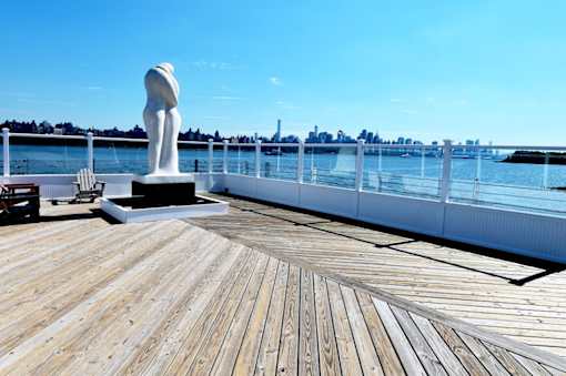 A statue of a naked man stands on a wooden deck overlooking a body of water.
