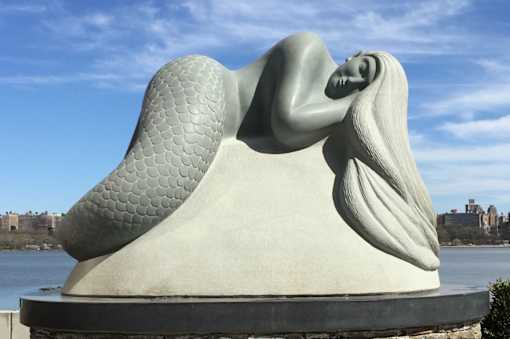 A sculpture of a woman with a fish scale pattern on her back is displayed outdoors.