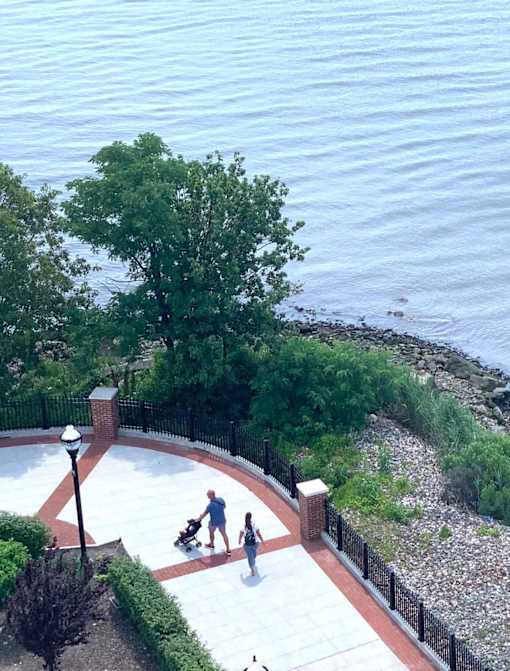 A couple walking with a baby in a stroller in a park near the sea.