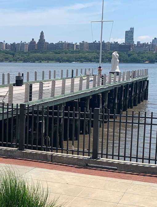 A pier with a statue on it and a city skyline in the background.