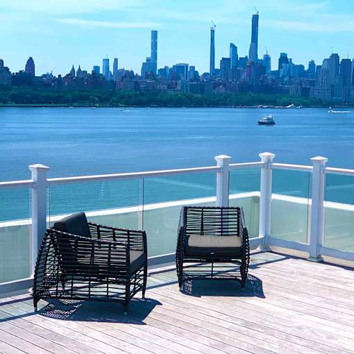 Two chairs are on a deck overlooking a body of water with a city skyline in the background.