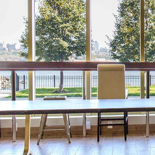 A long table with a chair and a view of a waterfront.