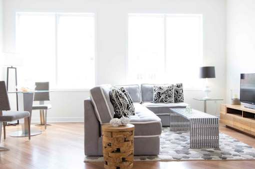 A modern living room with a grey sofa, a glass table, and a wooden floor.