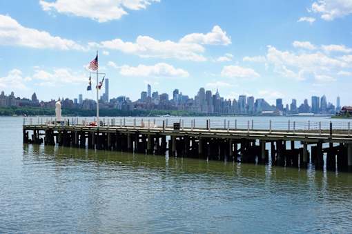 A pier with a flag and a city skyline in the background.