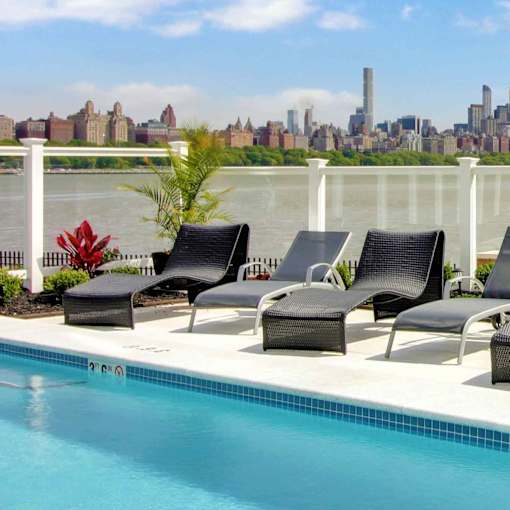 Four black chairs are arranged on a patio next to a pool.