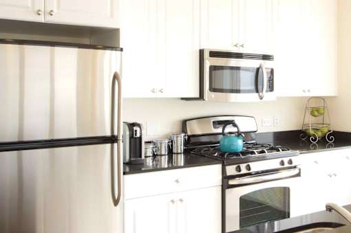A modern kitchen with a stainless steel refrigerator, a microwave above the stove, and white cabinets.