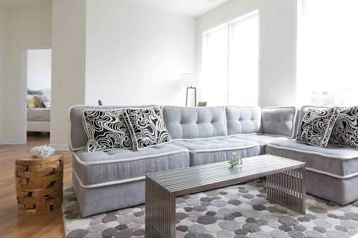 A grey sofa with a pillow and a glass table in front of it.